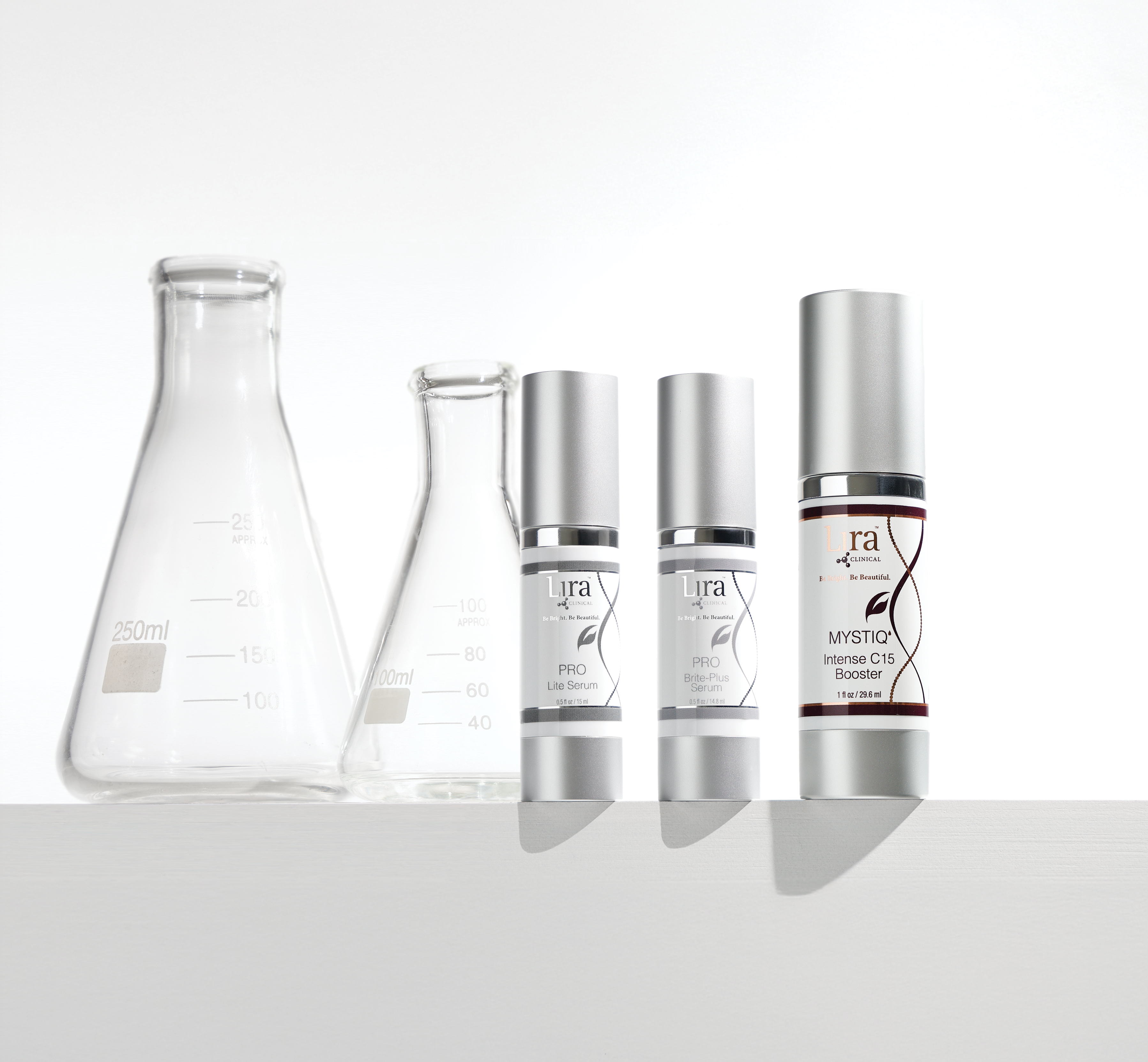 Two beakers in background Three products lined up Po Lite Serum Pro Brite-Plus Serum MYSTIQ Intense C15 Booster